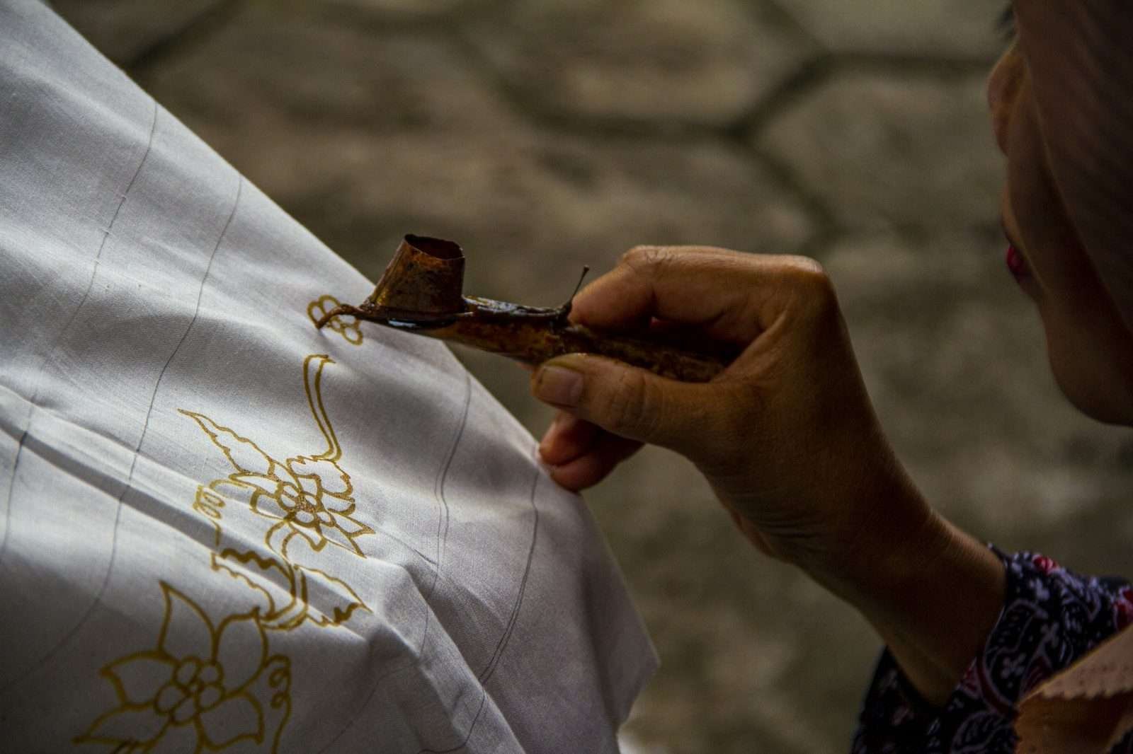 Illustrative image: hand drawing a batik design on fabric with a wax tool