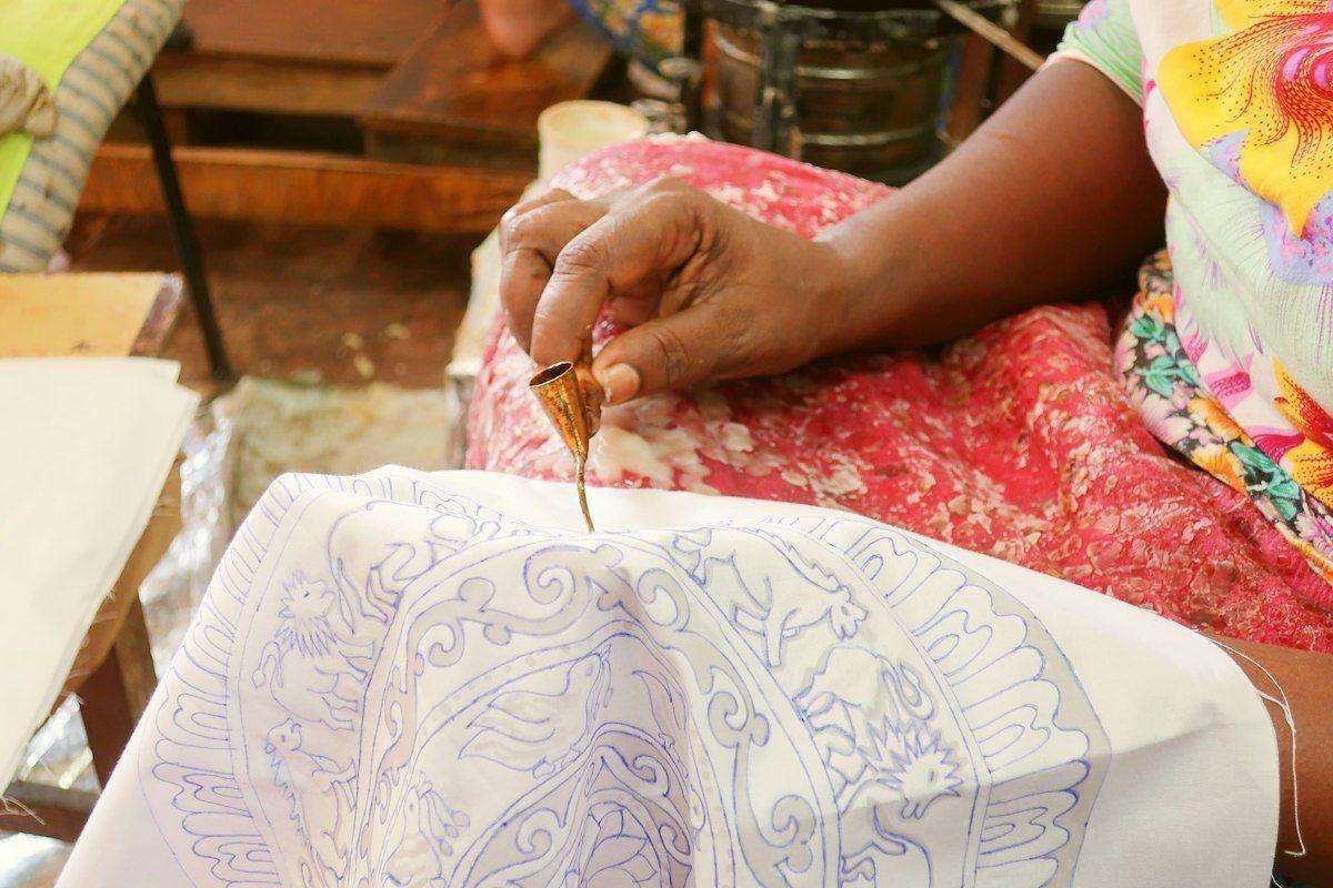 Illustrative image: hands applying wax to fabric with a tool