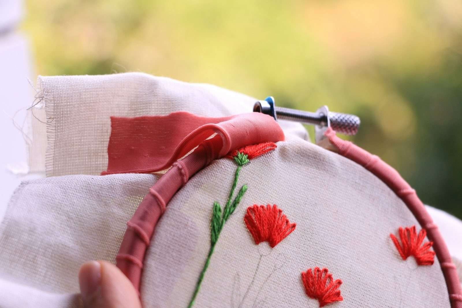 Illustrative image: hands embroidering red flowers on fabric in a hoop