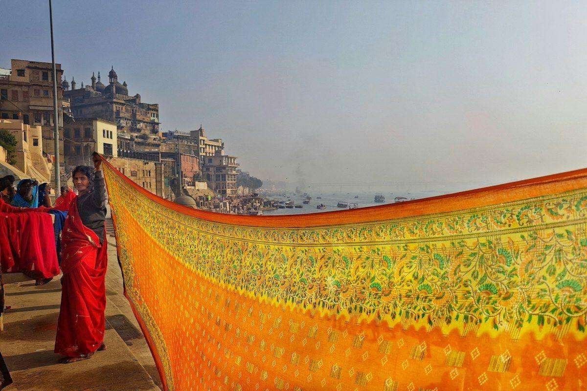 Illustrative image: a long printed saree held out to dry by a river