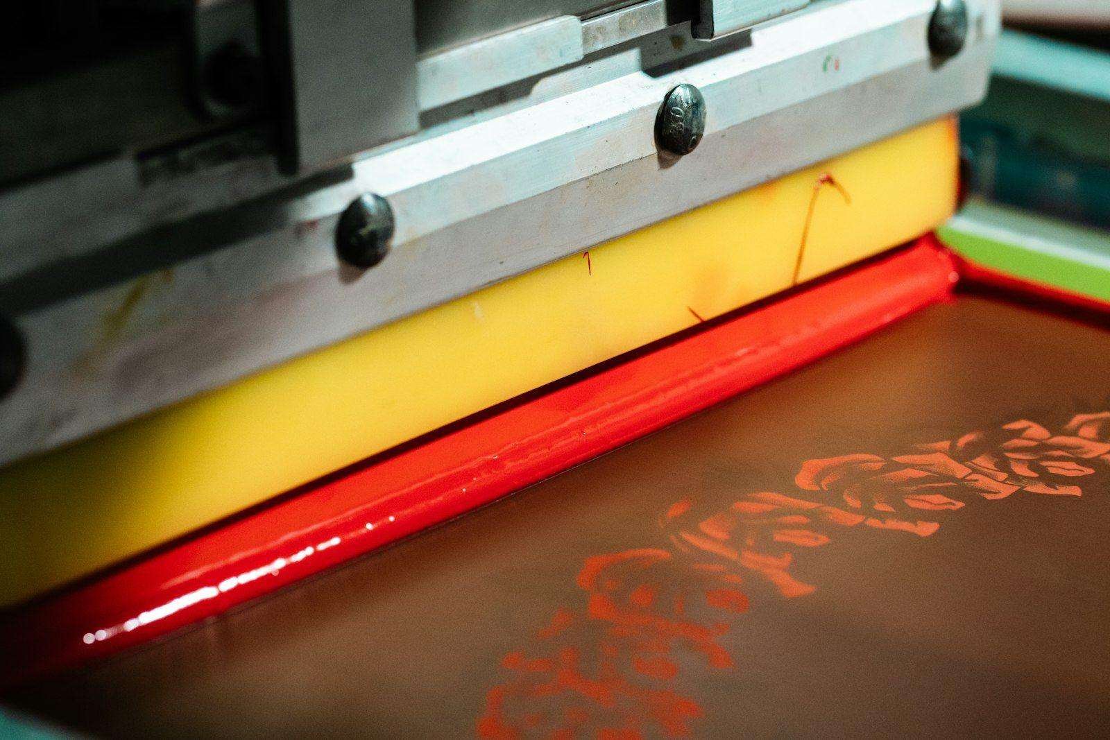 Illustrative image: close-up of machine screen printing with red ink